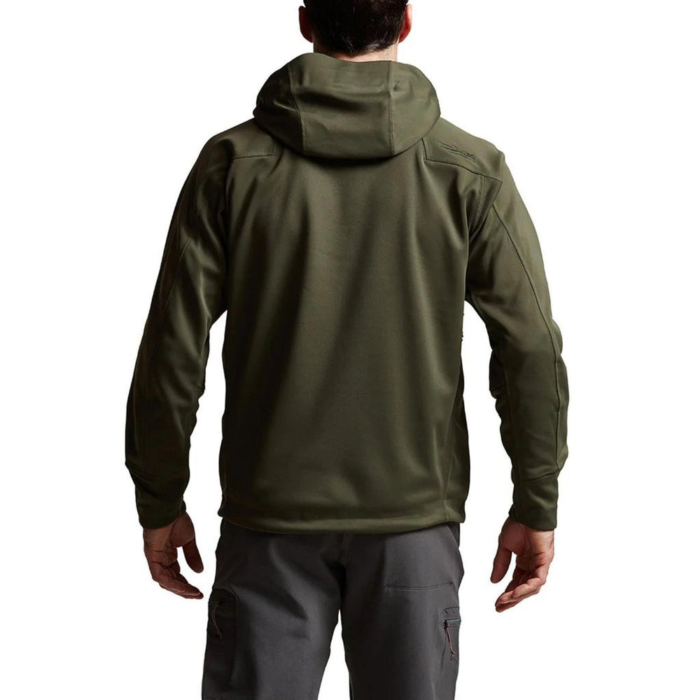 Model wearing the Deep Lichen Jetstream jacket photographed from behind, hood resting on the shoulders, paired with grey trousers.