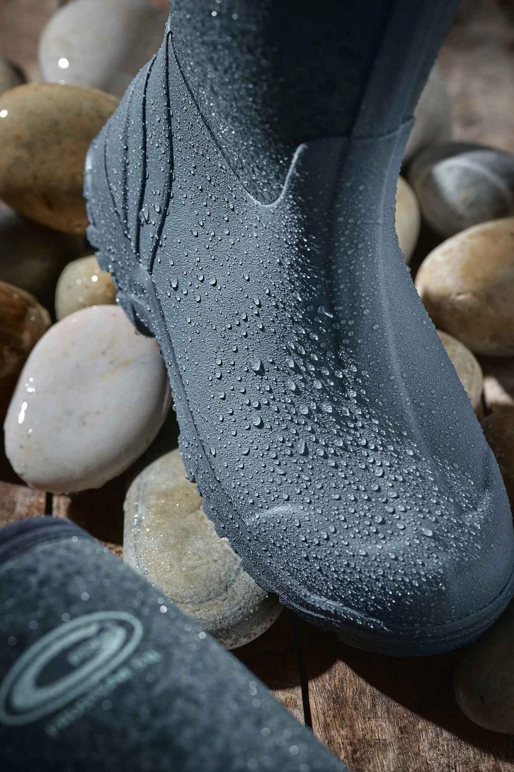 Toe and lower shaft of the grey Grubs Frostline 5.0 wellington boot beaded with water on wet pebbles