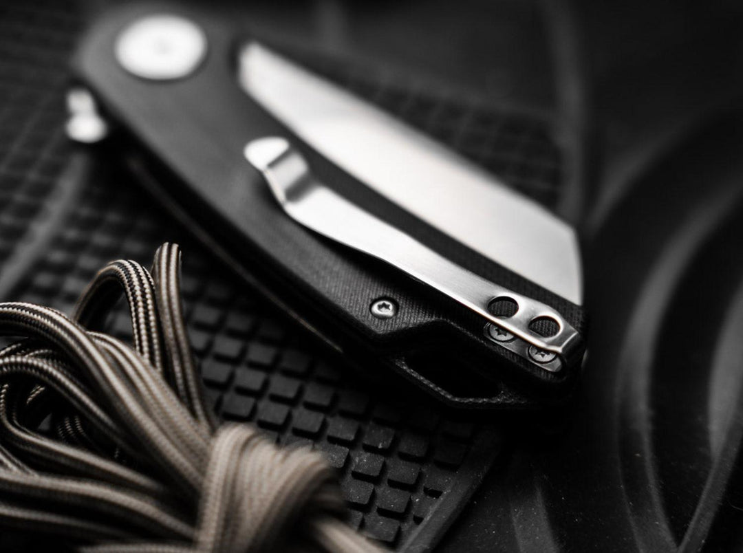 Close-up of the Böker Magnum Cliff Wharn folding knife with black handle and pocket clip lying on a rubber mat with cord