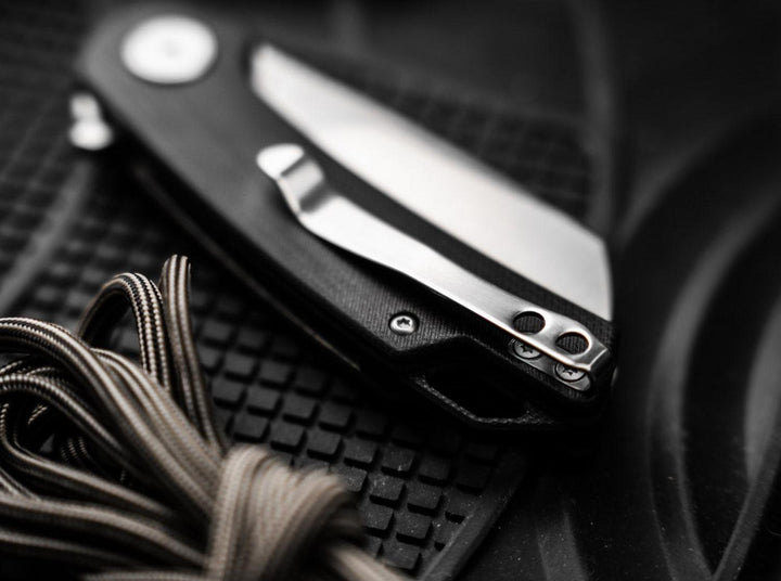Close-up of the Böker Magnum Cliff Wharn folding knife with black handle and pocket clip lying on a rubber mat with cord