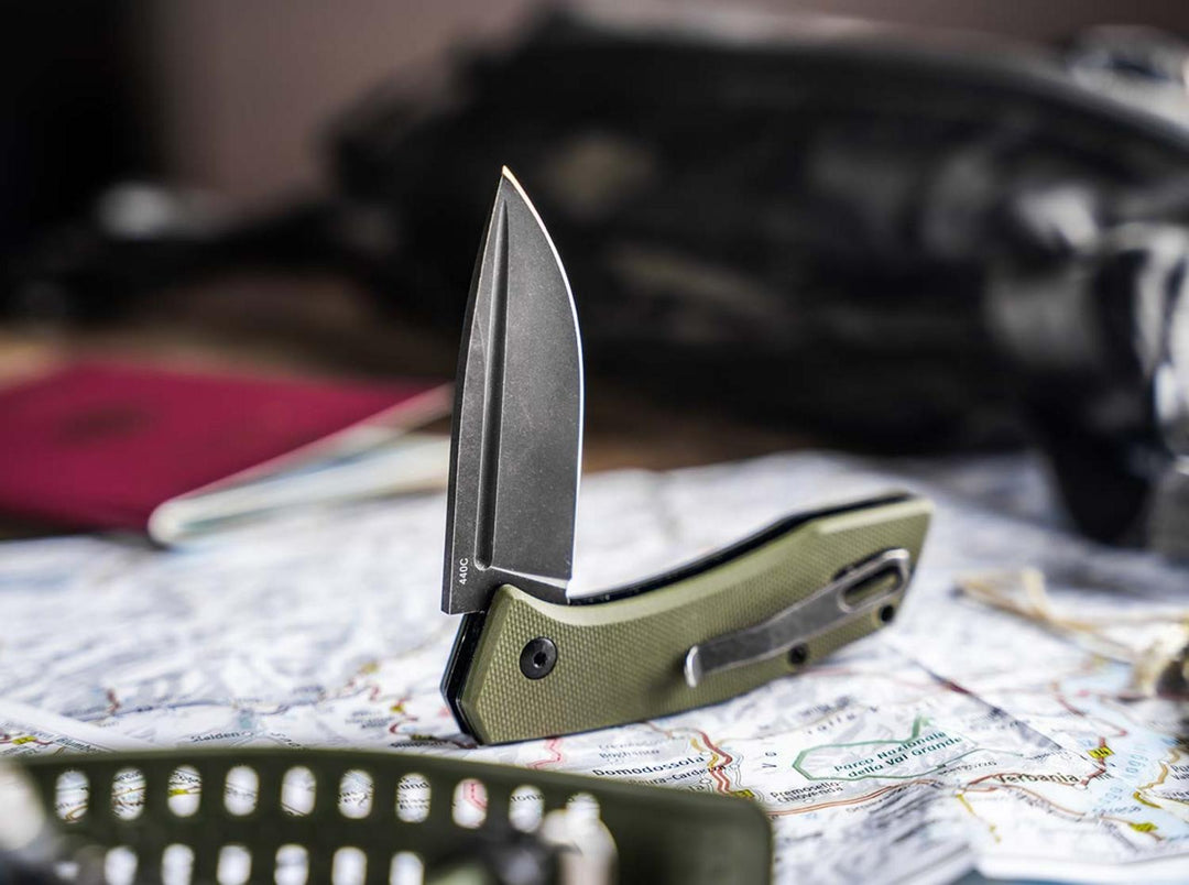 Böker Plus Worldwide 2.0 olive green folding knife standing open on a map beside travel gear, lifestyle shot