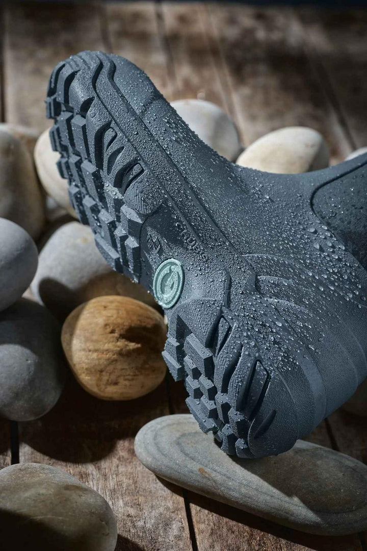 Sole of the grey Grubs Frostline 5.0 boot shown from below on wet pebbles, deep-lugged tread