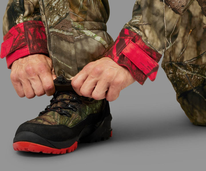 Hunter bending down to lace a camo hunting boot, with the gaiters and camo trousers above.