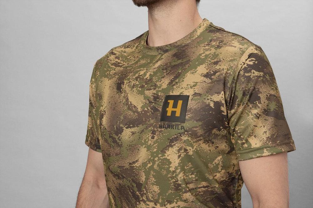 Cropped torso shot of a model wearing the camouflage t-shirt against a grey studio backdrop.