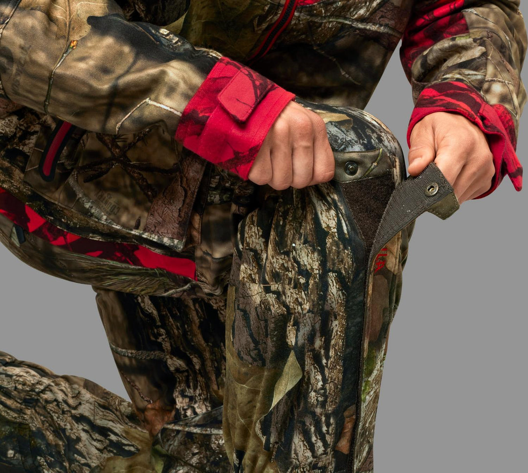 Hunter kneeling and peeling open the side closure of the gaiter, showing the hook-and-loop tab and inner storm flap.
