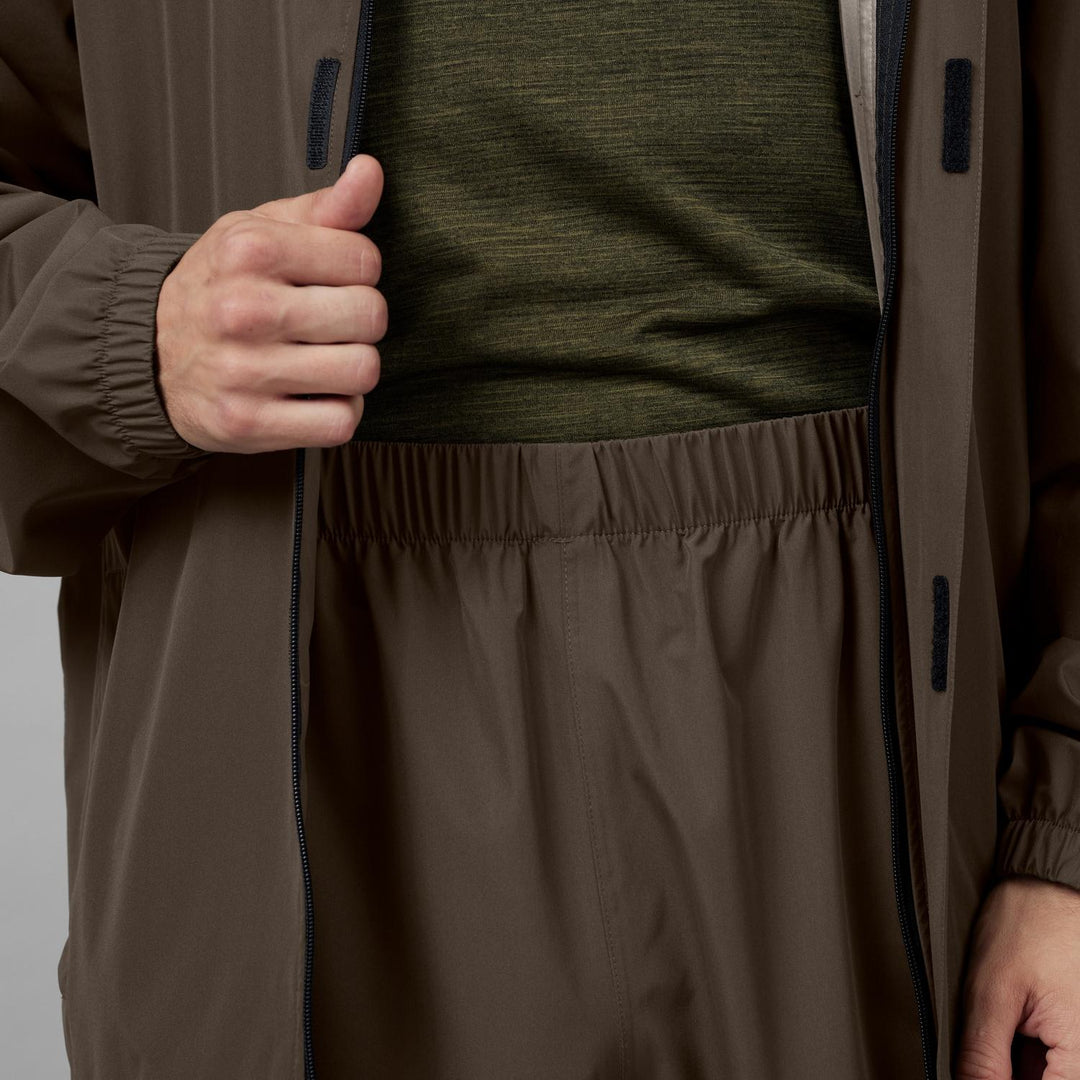 Close-up of the elasticated trouser waistband worn under the open jacket, taped seams and olive base layer visible