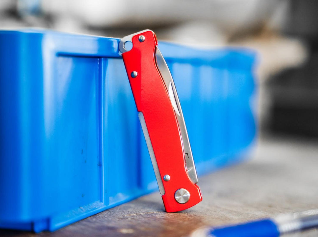 Red Böker Plus Atlas knife standing on edge against a blue storage bin on a workbench, lifestyle shot