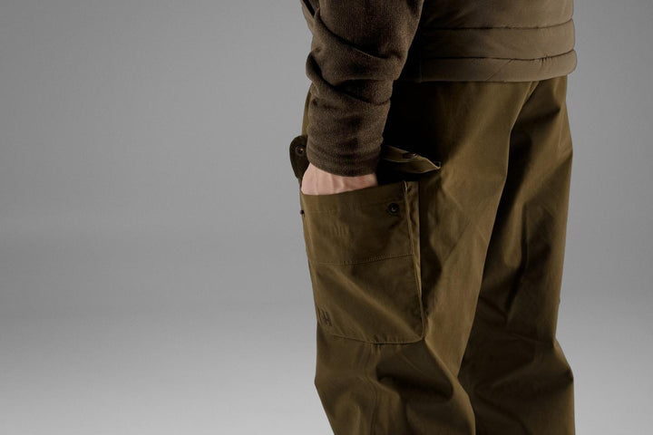 Side close-up of the Retrieve trousers' open cargo pocket and reinforced knee area on a model