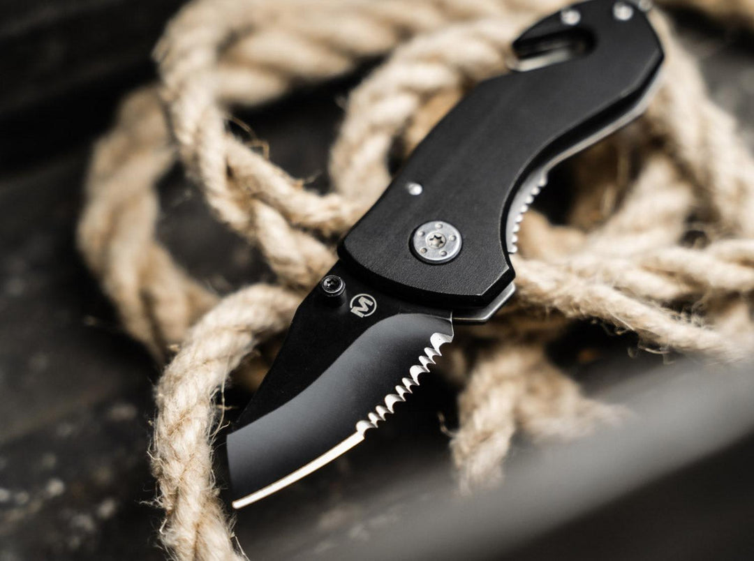 Böker Magnum Black Rescue folding knife with black serrated blade resting on coiled rope, lifestyle shot