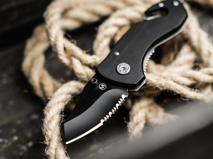 Böker Magnum Black Rescue folding knife with black serrated blade resting on coiled rope, lifestyle shot