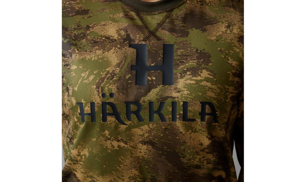 Close-up of the chest print on the Harkila Deer Stalker tee, showing the dark H monogram and HARKILA wordmark over the fine AXIS MSP Forest camo knit.