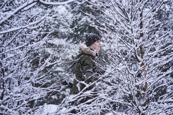 Lifestyle: woman in olive hunting kit walking through heavily snow-laden birch and spruce trees