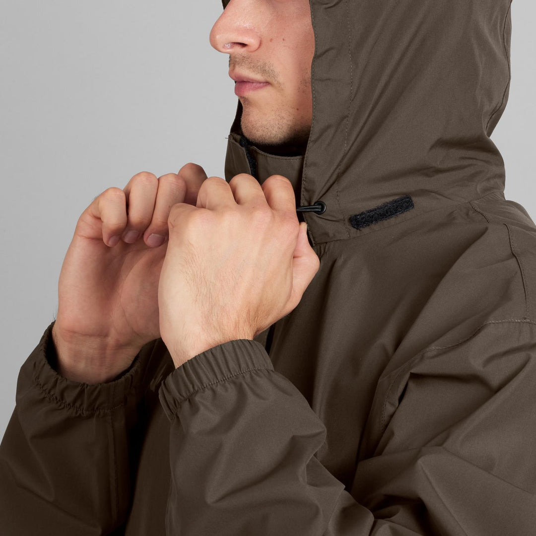 Model pulling the Taxus jacket's hood drawcord closed at the chin, close-up of the collar and elasticated cuff