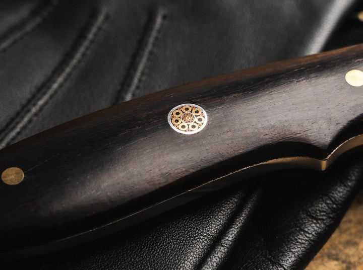 Close-up of the black handle with brass rosette inlay on the Böker Magnum Vernery Damascus knife on black leather