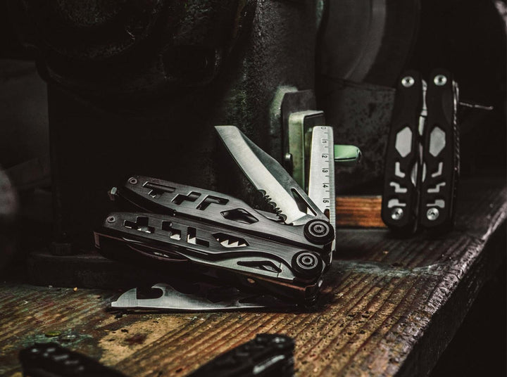 Lifestyle shot of Böker Plus Specialist II multitools on a dark workbench, one open with its blade extended