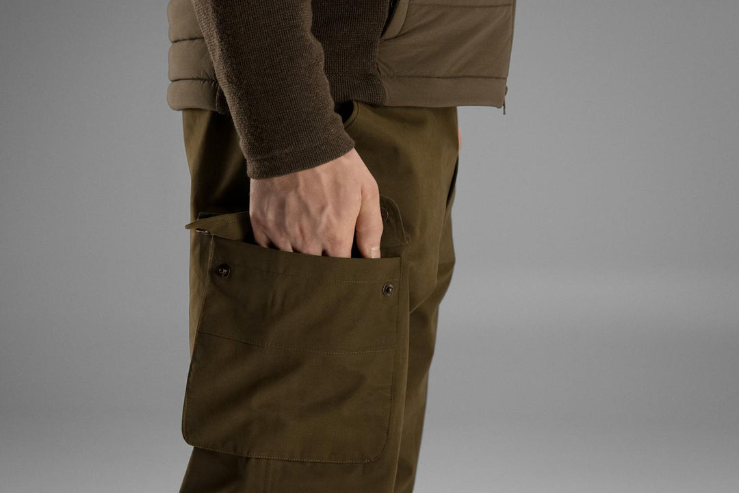 Close-up of a hand in the Retrieve trousers' bellows thigh pocket, worn with a fleece