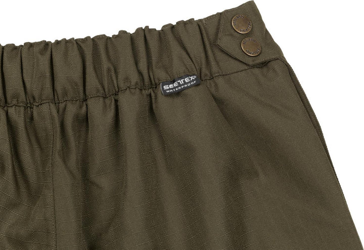 Close-up of the Buckthorn overtrouser waistband: elasticated olive fabric, woven Seeland label and two brass press studs