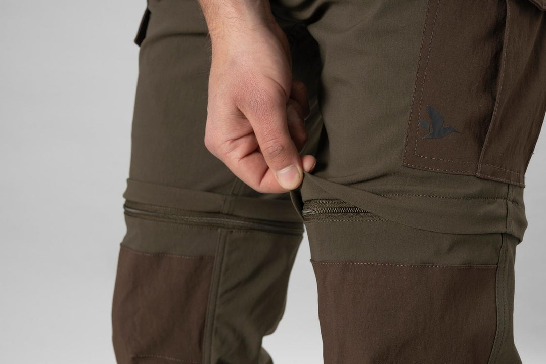 Model pulling the zip-off leg section away at the knee, showing the trousers converting to shorts