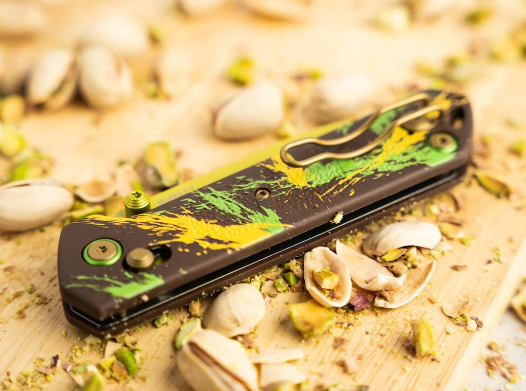 Böker Plus Kihon Dubai Chocolate folding knife closed on a wooden board among pistachio shells, lifestyle shot