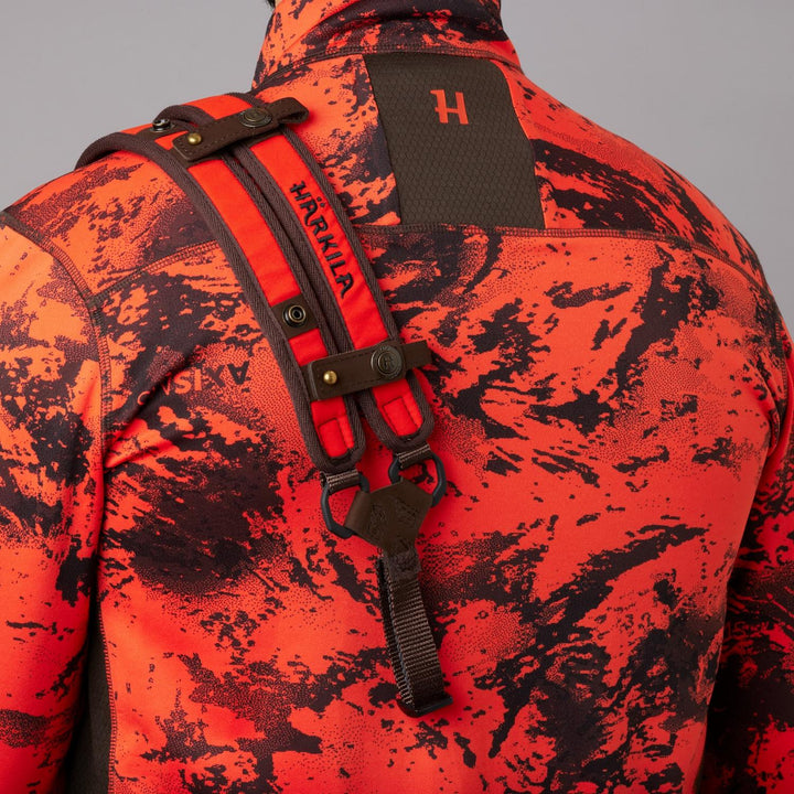 Härkila Wildboar Pro sling worn over a blaze camo jacket, close-up of the padded shoulder strap and the black plastic connector on the chest.