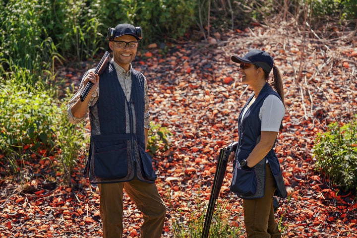 Lifestyle: man and woman with shotguns and navy Seeland Skeet II waistcoats standing in autumn woodland
