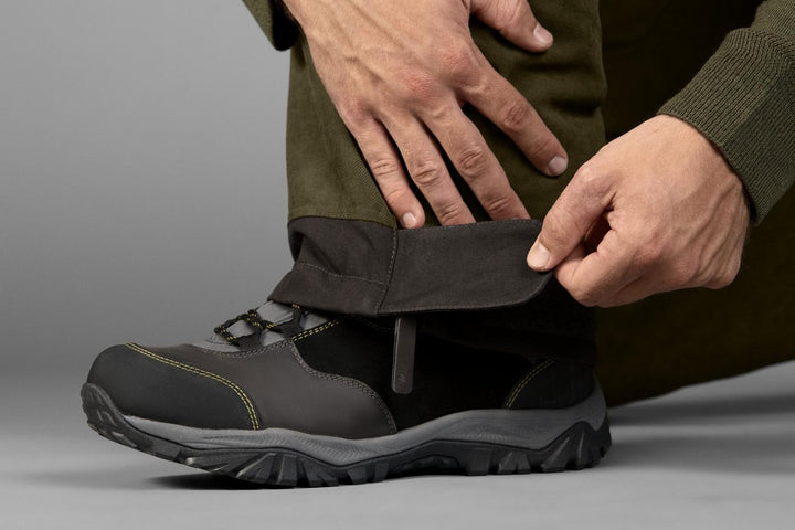 Close-up of hands securing the ankle cuff of the Seeland Taiga trousers over a boot
