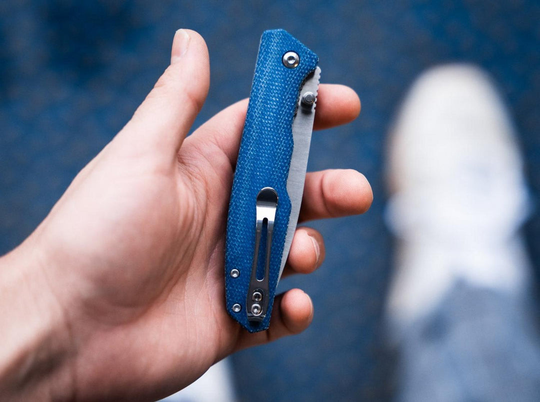 Hand gripping the closed blue canvas Böker Magnum folding knife, showing the pocket clip, lifestyle shot