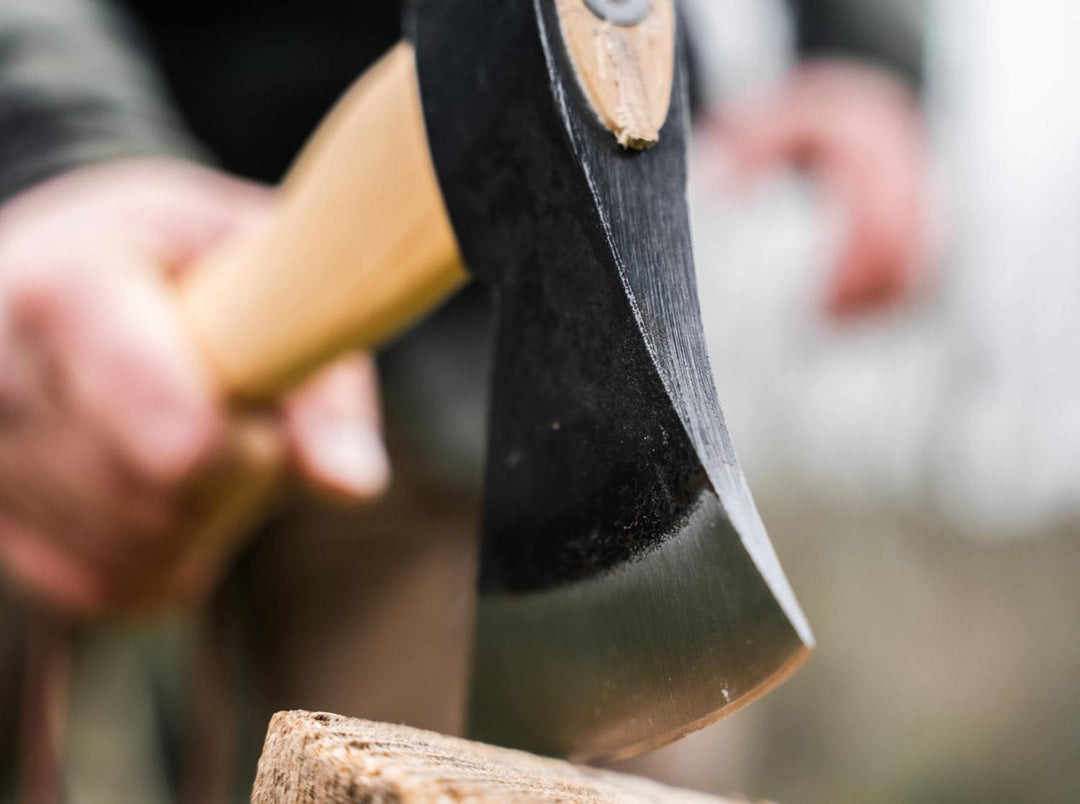 Lifestyle shot of a hand gripping the Böker Plus Appalachian Origin axe with the blade resting on a log outdoors