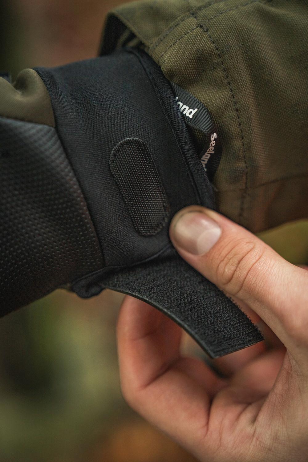 Fingers lifting the hook-and-loop wrist strap on the glove cuff to show the adjustable closure and perforated grip panel.