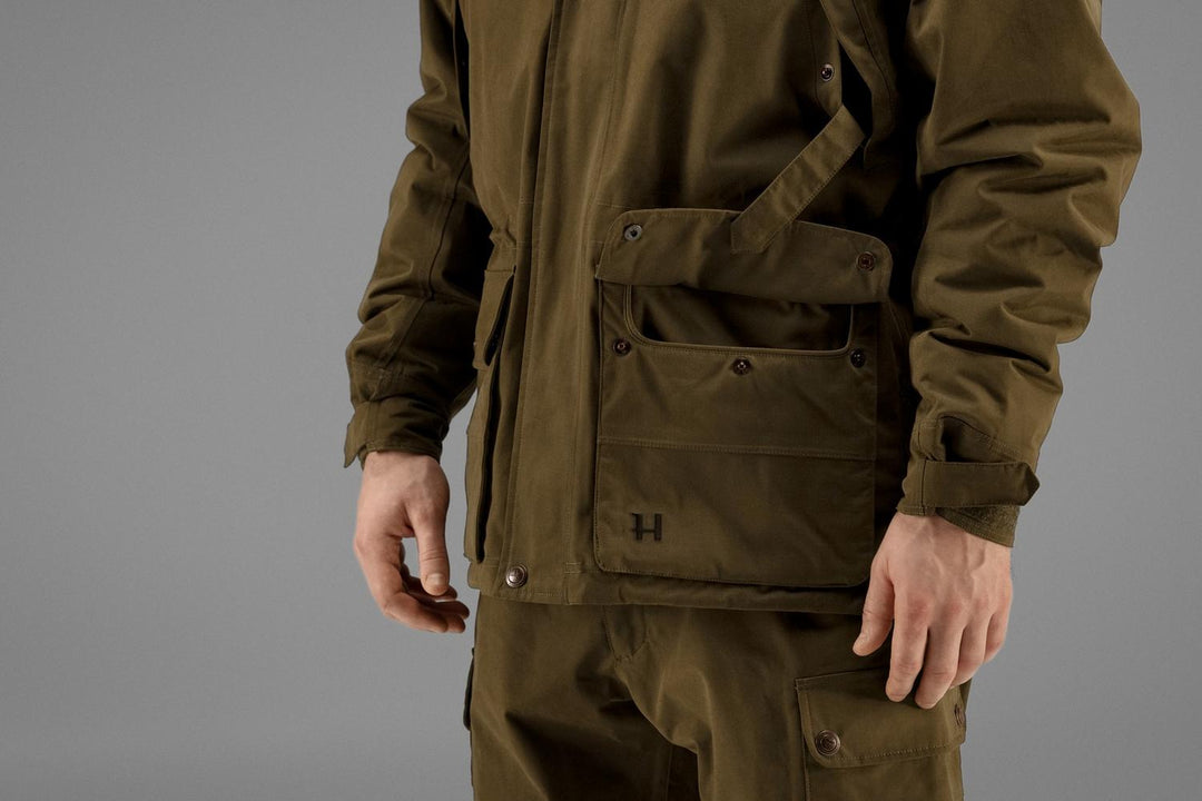 Side detail of the Härkila Retrieve jacket showing the bellows cargo pocket on the hip, the H logo tab and the adjustable cuff