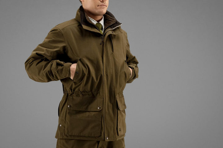 Close-up of a model in the Härkila Retrieve jacket, three-quarter front, collar turned up over a shirt and tie with the front zip open