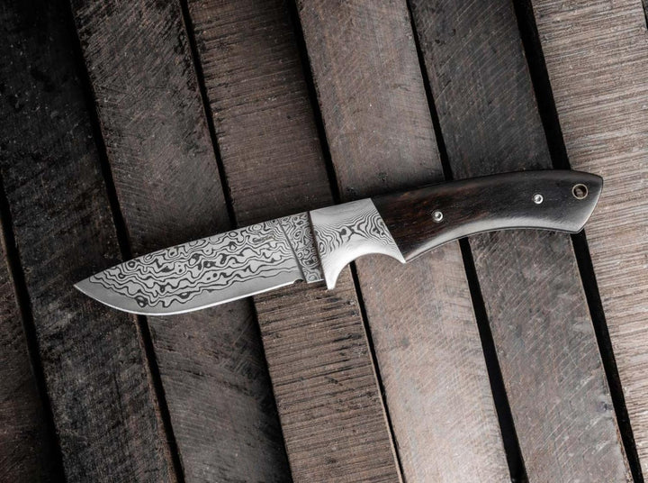 Böker Plus M-One Damascus fixed blade hunting knife lying on rustic dark wooden planks, lifestyle shot