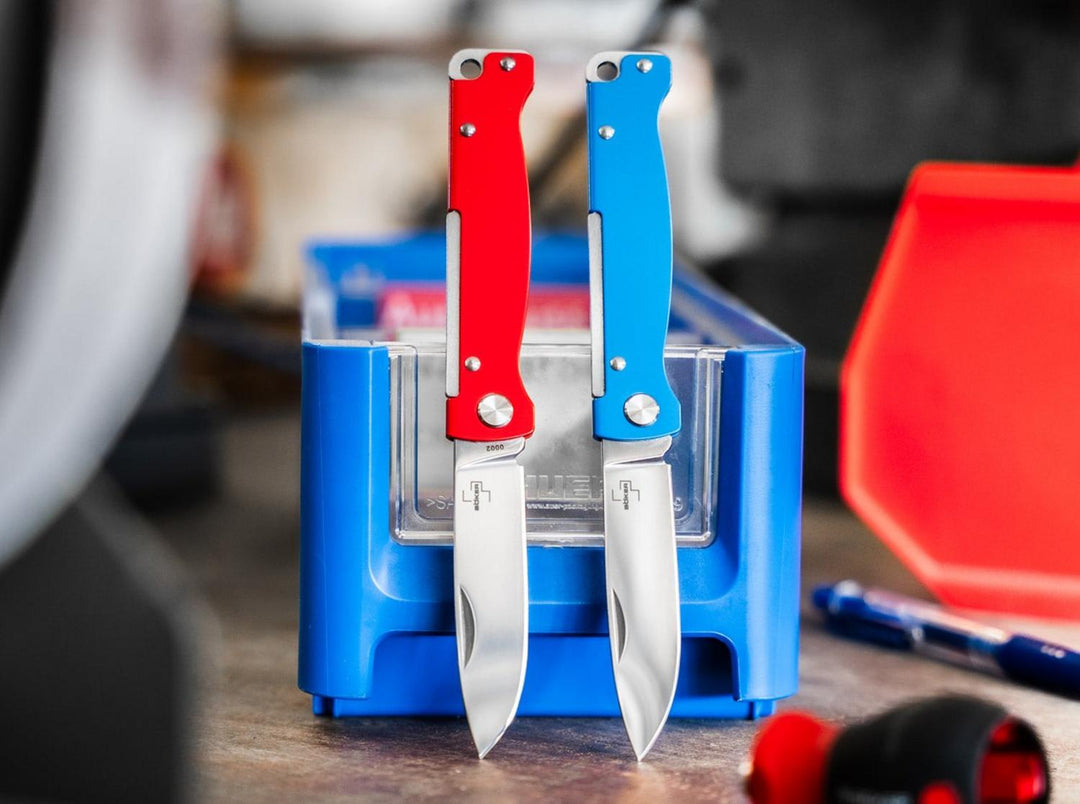 Red and blue Böker Plus Atlas knives standing upright in a blue parts bin, lifestyle shot