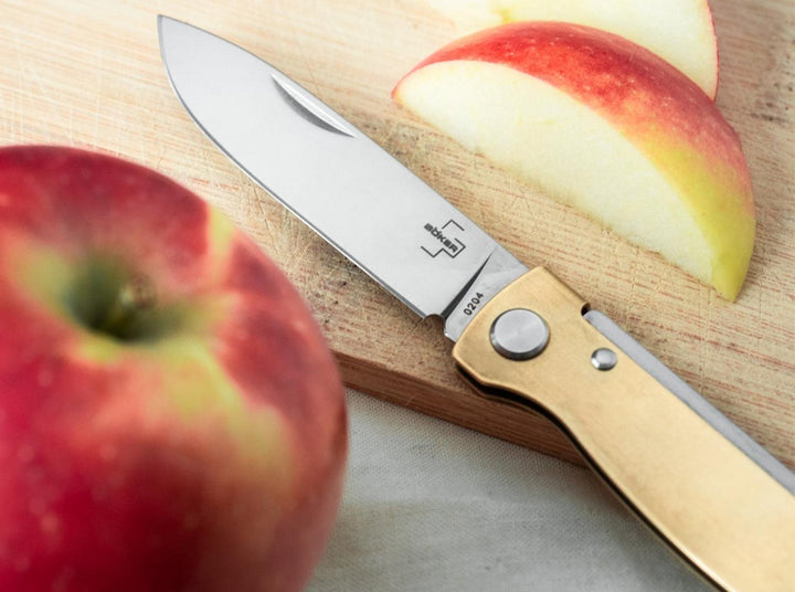 Böker Plus Atlas Brass knife beside cut apple on a wooden board, lifestyle shot