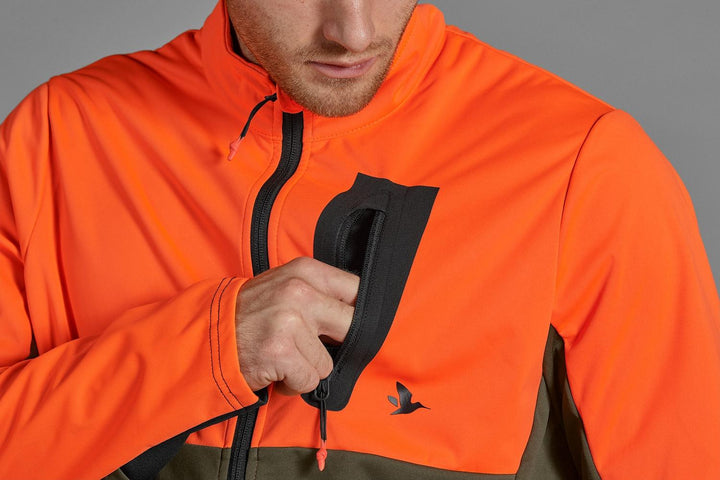 Seeland Force Advanced softshell jacket in blaze orange and dark olive – view 3: close-up of a hunter adjusting the hem drawcord toggle at the jacket's side.