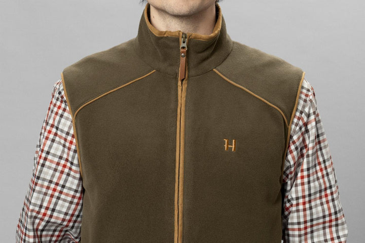 Close-up front view of the olive Härkila Sandhem 200 waistcoat on a model, showing the full-length zip and copper H logo