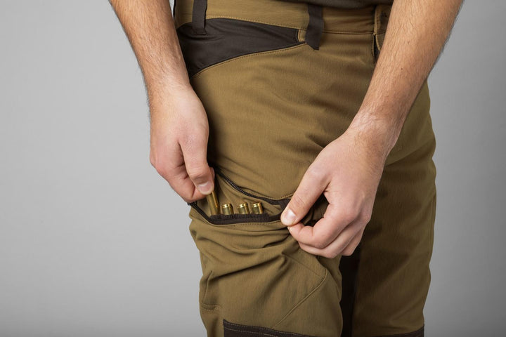 Close-up of the Härkila Ragnar trouser waistband with a hand slotting brass rifle cartridges into the integrated cartridge loops