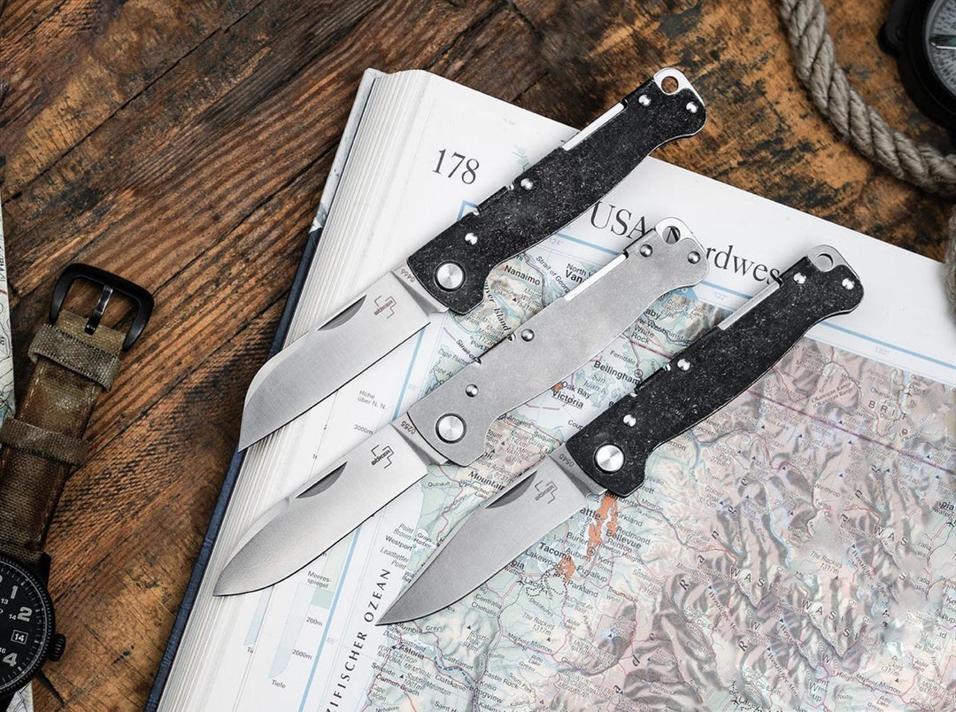 Three Böker Plus Atlas folding knives lying open on a map and wooden table, lifestyle shot