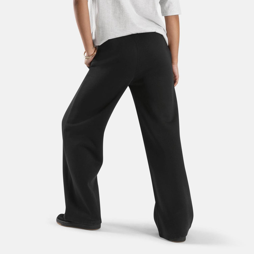 Model in the black fleece wide-leg pants, rear three-quarter view showing the loose straight leg and full-length drape