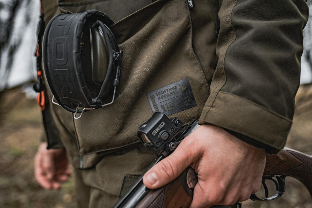 Lifestyle detail: a shooter in the Seeland Trax jacket carrying a broken shotgun, with ear defenders slung across the chest