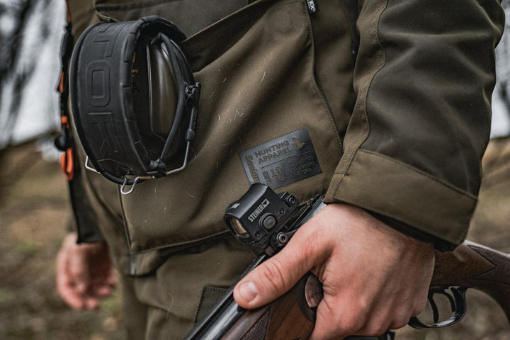 Lifestyle detail: a shooter in the Seeland Trax jacket carrying a broken shotgun, with ear defenders slung across the chest