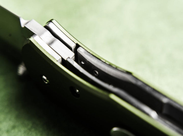 Close-up detail of the Böker Plus Lefti olive green handle and lock area against a green background