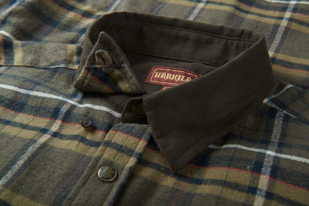Close-up of the Harkila Pajala shirt collar, dark green moleskin trim with the red woven Harkila label and a press-stud placket.
