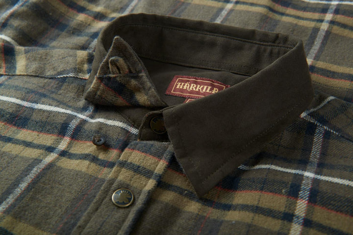 Close-up of the Harkila Pajala shirt collar, dark green moleskin trim with the red woven Harkila label and a press-stud placket.