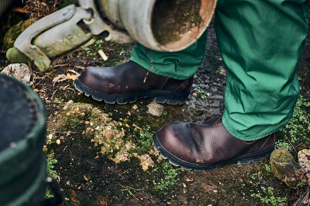Grubs Whirlwind brown leather dealer boots worn with green trousers on mossy, muddy ground by a farm trough