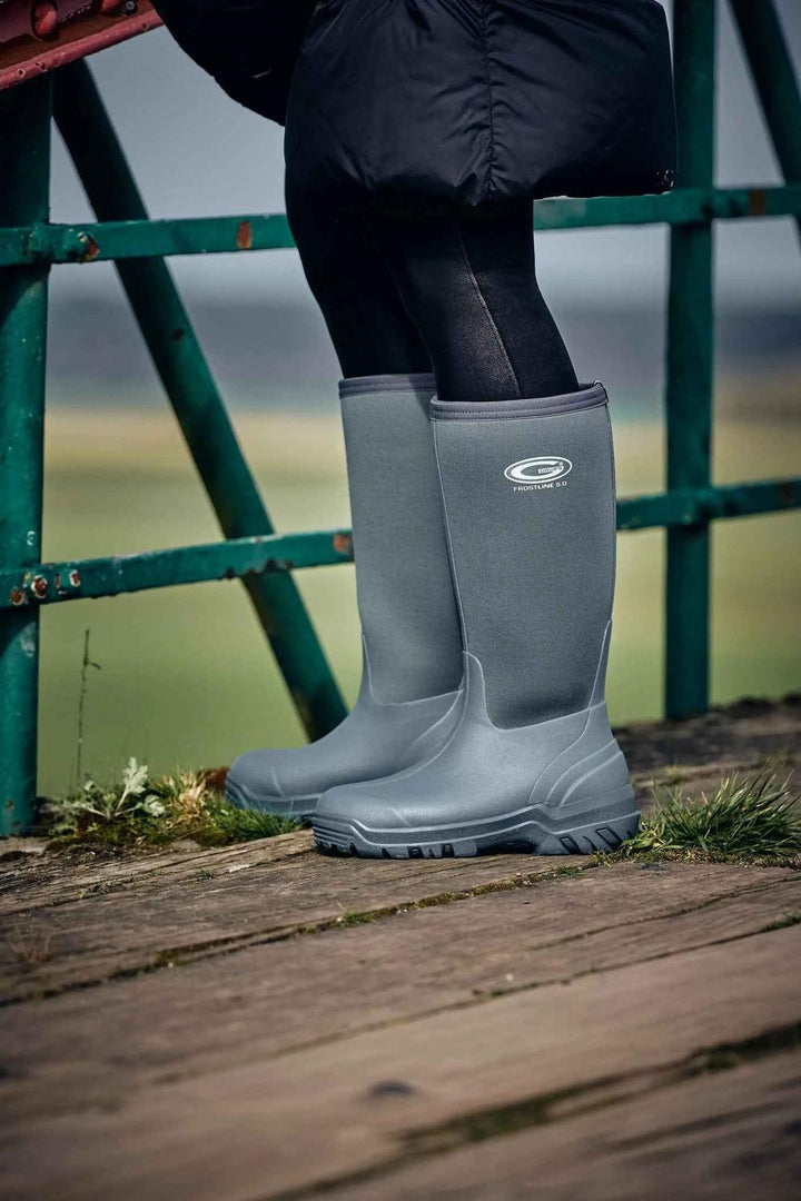 Person wearing grey Grubs Frostline 5.0 insulated wellington boots standing by green railings