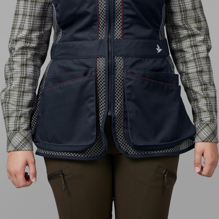 Model wearing the navy Seeland Skeet II Lady waistcoat over a check shirt, front torso view showing the red-piped lower pockets and the Seeland bird logo