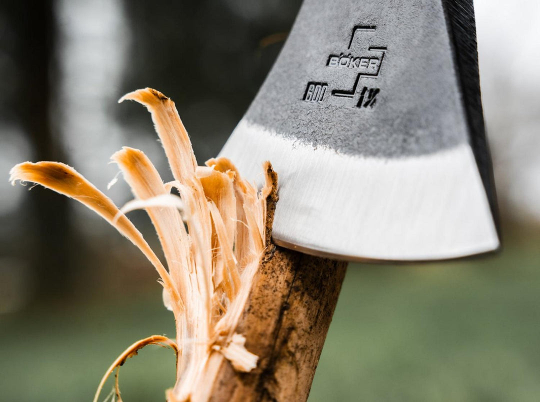Close-up of the Böker Plus Appalachian Origin axe head with Böker logo, splitting a branch and throwing wood shavings