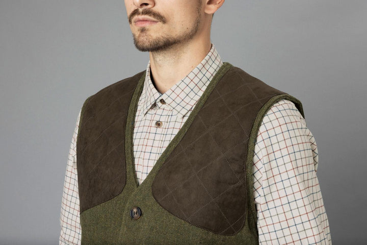Studio three-quarter chest view on grey, waistcoat worn over a tattersall check shirt showing the brown suede shooting patch and horn button.