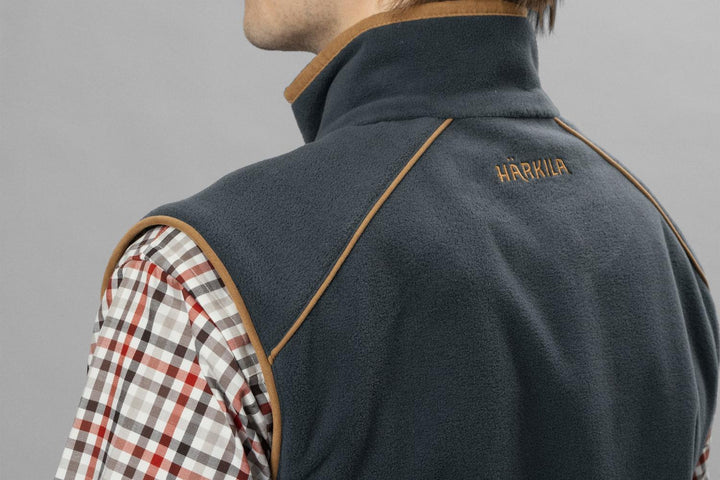 Close-up of the collar and shoulder of the navy Härkila Sandhem 200 waistcoat worn over a red check shirt, showing the tan piping and HARKILA embroidery